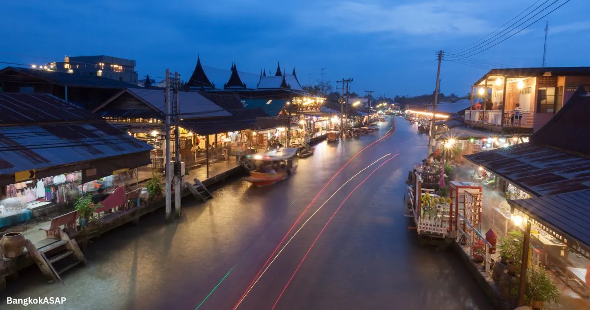 Lit shopfronts and boats reflected in the Amphawa canal at dusk, near Bangkok