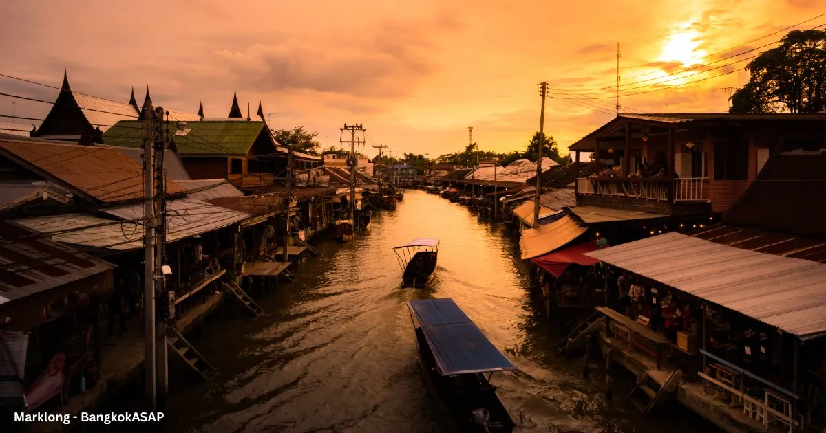 Longtail boat on the Amphawa canal at sunset, wooden houses along both banks
